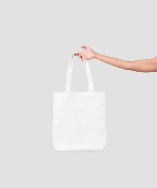 Photo of hand holding bag canvas fabric for mockup blank template isolated on gray background.