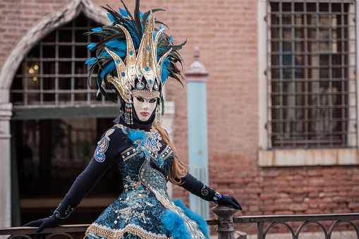 A DSLR photo of Venetian Carnival mask in Venice, Italy. The mask isthe main focus of the picture.The masks has multi coloured parts with feathers and decorations.