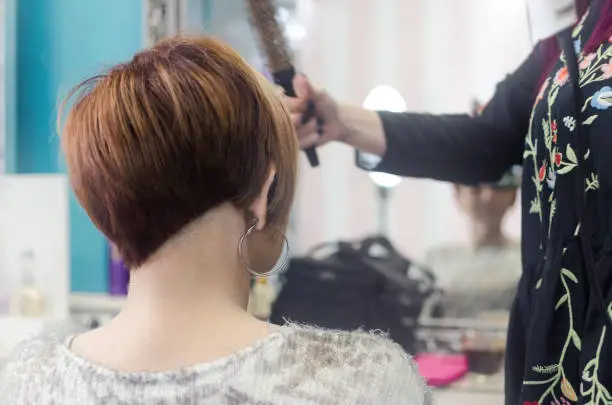 Photo of hairdresser loves the customer in the salon, woman sits on a chair facing back and imposes a new haircut