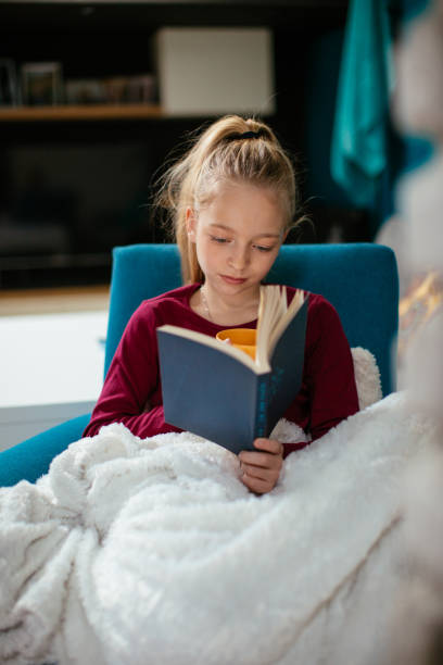 istock Smart girl reading book in living room 918334878