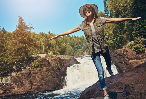 Shot of a young woman having fun next to a rocky river and waterfall