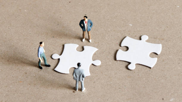 istock Three miniature men staring down two pieces of the puzzle. 918338138
