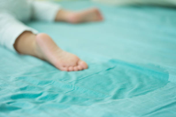 i piedi del bambino e fare pipì in un materasso. piedini e pipì in lenzuolo la mattina. concetto di sviluppo del bambino. - enuresis foto e immagini stock