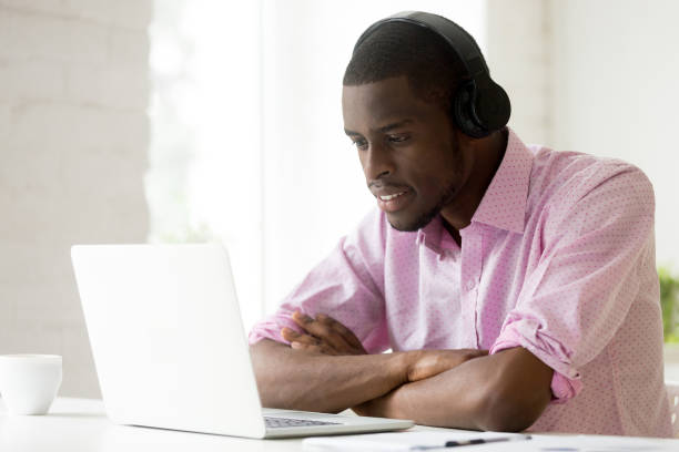 hombre afroamericano con usando laptop mirando la pantalla del ordenador auriculares - digital enhancement audio fotografías e imágenes de stock