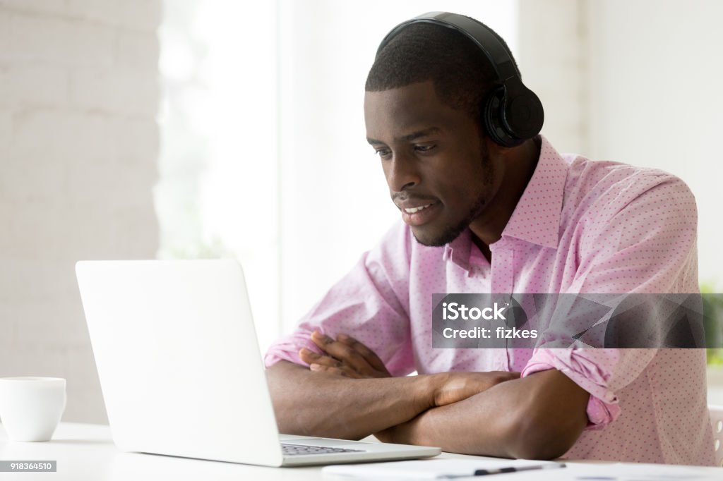 Uomo afro-americano che indossa le cuffie usando il laptop guardando lo schermo del computer - Foto stock royalty-free di Corso di formazione