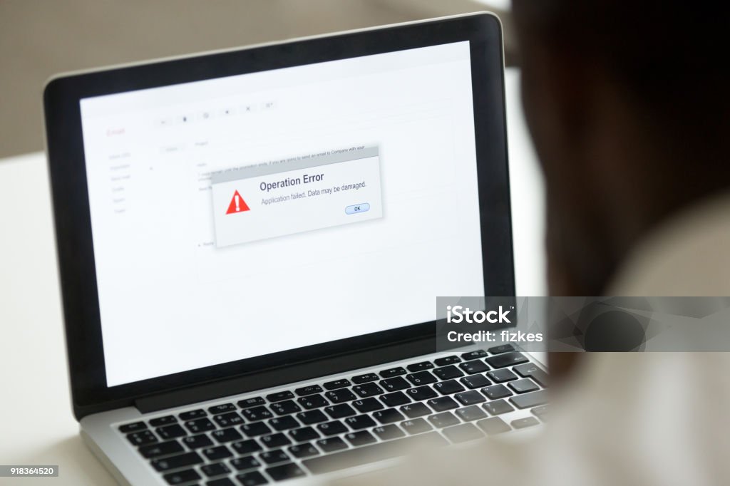 African man using laptop with application failure message on screen Computer error failure concept, african man using laptop with application failure message on screen, bad software pc app crash, email malware, data loss and recovery, rear view over the shoulder Error Message Stock Photo