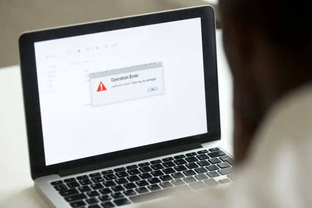 Computer error failure concept, african man using laptop with application failure message on screen, bad software pc app crash, email malware, data loss and recovery, rear view over the shoulder