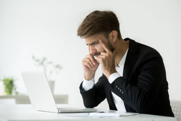 istock Businessman squinting eyes trying to focus looking at laptop screen 918364616