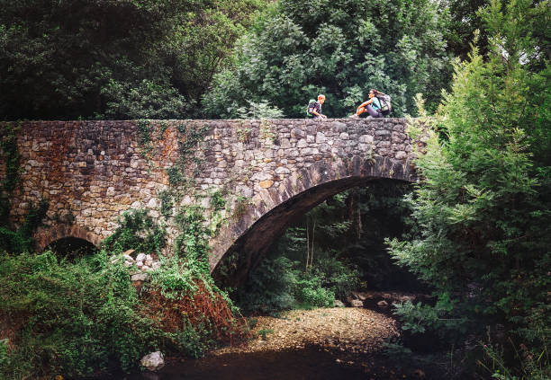 mutter und sohn sitzen auf alten viadukt brücke über den fluss wald - pilgrimage stock-fotos und bilder