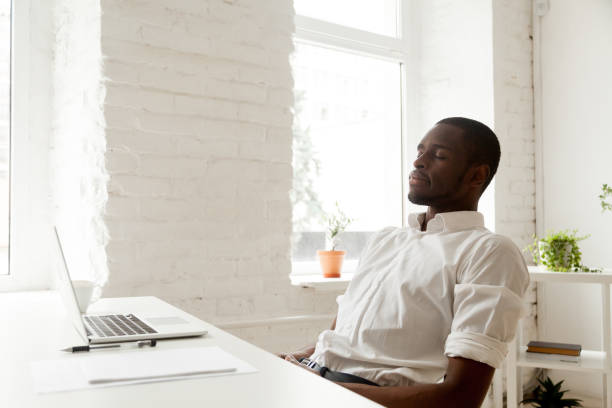 African-american man relaxing after work breathing air in home office African american man relaxing after work breathing fresh air sitting at home office desk with laptop, black relaxed entrepreneur meditating with eyes closed for increasing productivity at workplace eyes closed stock pictures, royalty-free photos & images