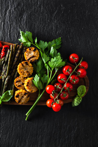 istock grilled vegetables on a wooden tray on a black slate. copy space 918365254