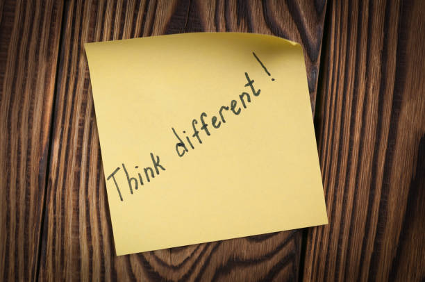 istock Black handwritten inscription Think different on yellow square sticky sticker on old wooden brown table. Business concept 918366480