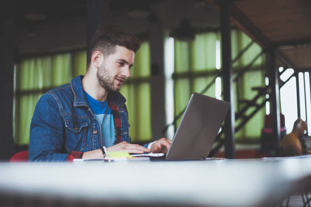 istock Young businessman working in office, sitting at desk, looking at laptop computer screen, smiling 918368672