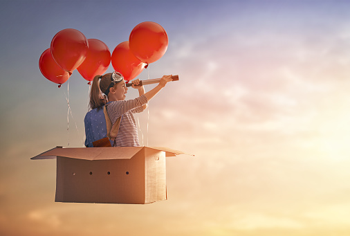 Dreams of travel! Child is flying in cardboard box with air balloons.