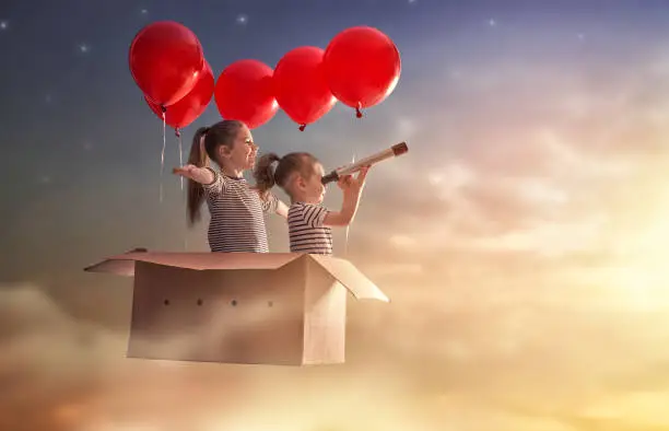Dreams of travel! Two children are flying in cardboard box with air balloons.