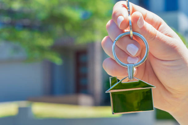 istock Hand holding a house key in front of a large house. 918374536