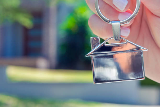 istock Hand holding a house key in front of a large house. 918374540