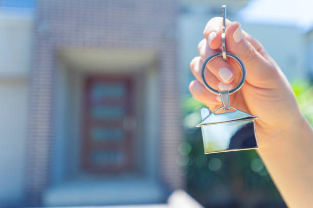 istock Hand holding a house key in front of a large house. 918374542