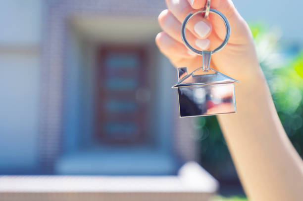 istock Hand holding a house key in front of a large house. 918374544