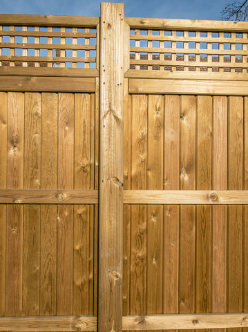 Wooden fence panelling with fancy top, golden in color and sunlit