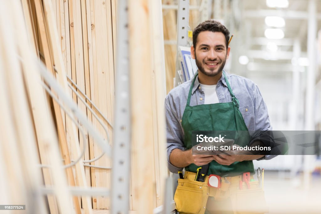 Confident man working in lumber yard Handsome young Hispanic man works in a lumber yard. He is holding a digital tablet while smiling at the camera. Hardware Store Stock Photo