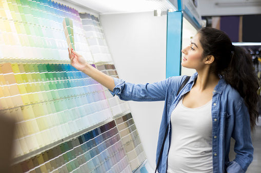 Young Middle Eastern woman compares several paint colors while shopping for paint in home improvement store.