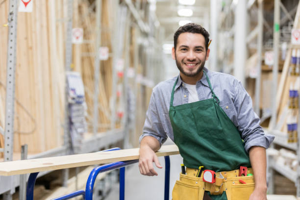 Confident hardware store employee Portrait of handsome Hispanic male hardware store employee leaning on a dolly as he works with lumber. lean construction management stock pictures, royalty-free photos & images
