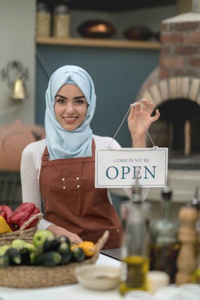 istock Arab woman working at a restaurant and holding an open sign 918377632