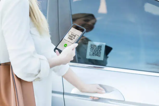 Unrecognizable woman uses ride share app. She is scanning a QR code before getting into the car.