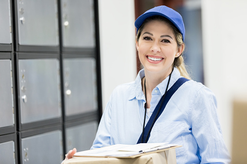 Cheerful mid adult Caucasian female mail carrier prepares to place mail in mail boxes. The mail boxes are in the background.