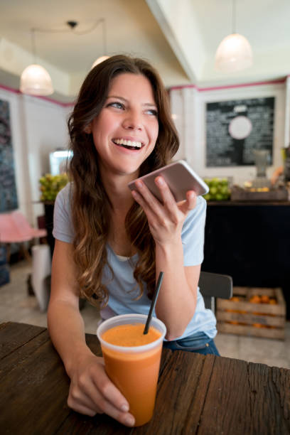 istock Beautiful young customer talking on her smartphone using the speakerphone looking very happy while enjoying a fresh juice at a juice bar 918381920