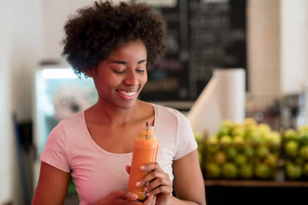 cliente feminino em um juice bar beber um suco de cenoura gostoso olhando muito feliz e sorridente, mantendo-a com as duas mãos - carrot juice - fotografias e filmes do acervo