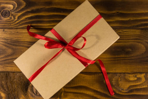 istock Cardboard gift box with red ribbon on wooden table 918396388