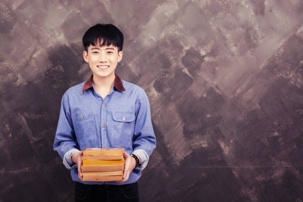 istock Handsome young asian man holding book on the grunge wall smiley looking at camera 918399294