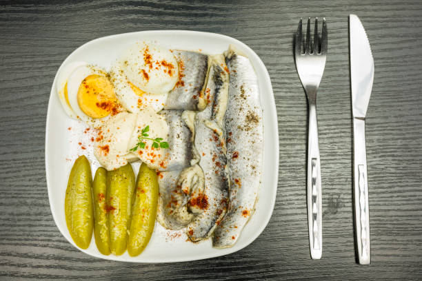 istock White plate with marinated herring in oil, boiled hard-boiled egg, cucumber and mayonnaise. Seasoned with black pepper and red paprika. View from above. 918399524