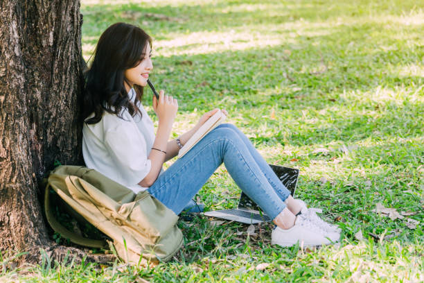 istock Woman with pen writing on a notebook sitting on grass in park 918406998