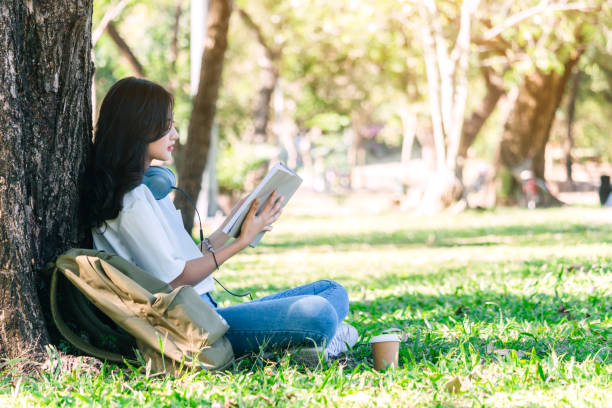 istock Students young woman relax and reading a book sitting on grass in park 918407332