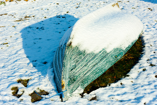 Small upside down rowboat partly covered in thawing snow.