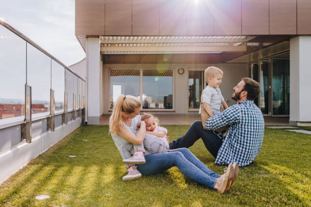 Happy family playing on the grass in front of their penthouse. Playful parents and their kids having fun while spending a day together on a penthouse balcony. apartment balcony garden stock pictures, royalty-free photos & images