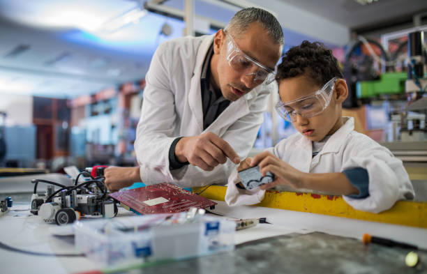 African American boy and his teacher working on computer part in laboratory. Mid adult teacher and small black boy cooperating while working in laboratory. school science project stock pictures, royalty-free photos & images