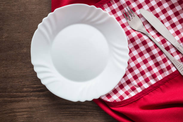 istock Clean, empty, white plate, fork and knife with tablecloth or towel on the brown rustic wooden table. Cutlery concept. Flat lay. Top view. 918421636