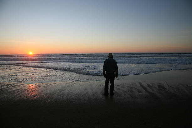A man steps into the breaking waves in the line of the rising sun to use his phone to take photos. This image was taken on Bondi Beach, Sydney on a cold and sunny morning at sunrise on 4 August 2024.