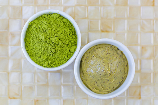 Fine Ground Japanese Matcha green tea leaves powder next to Green tea scrub with walnut shell and Cocoa exfoliator, top view