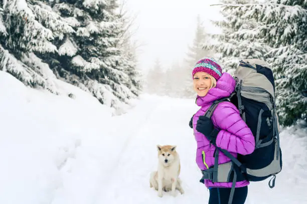 Woman hiking in white winter forest woods with akita dog. Recreation fitness and healthy lifestyle outdoors in nature. Motivation and inspirational winter landscape.