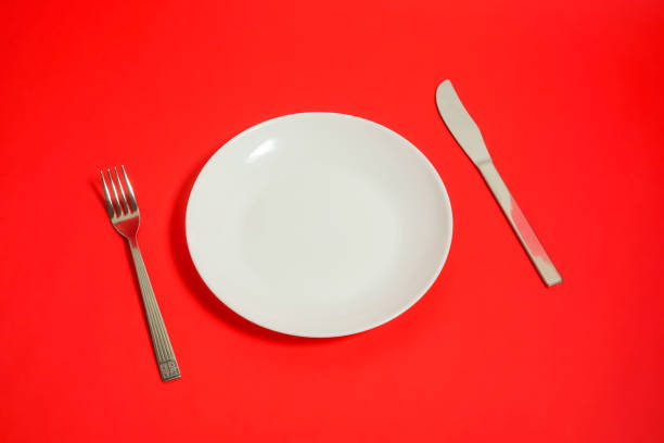 istock a white dish and a folk and a knife. restaurant image. red background. 918458748