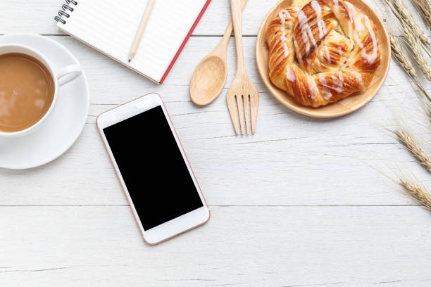 istock Top view danish pastries, coffee, note book and smartphone on white wooden table 918459100