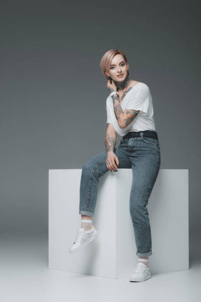 istock beautiful young woman with tattoos sitting on white cube and looking at camera on grey 918462980