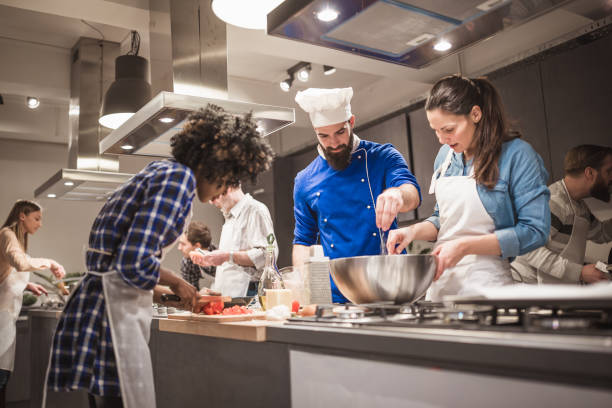 Young chef assisting a cooking class and explaining some tips and tricks Chef is supervising attendees of cooking class while they are making meals cooking class photos stock pictures, royalty-free photos & images