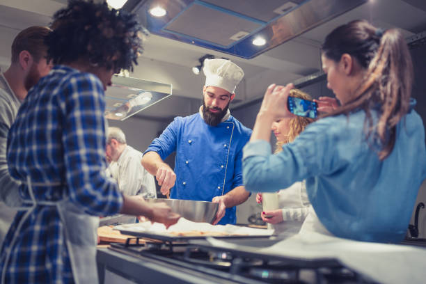 Chef assisting a cooking class, explaining some tips and tricks Chef is supervising attendees of cooking class while they are making meals. They are taking photographs with him cooking show stock pictures, royalty-free photos & images