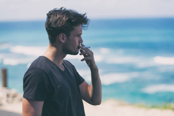 Young attractive man smoking cigar on the beach. stock photo
